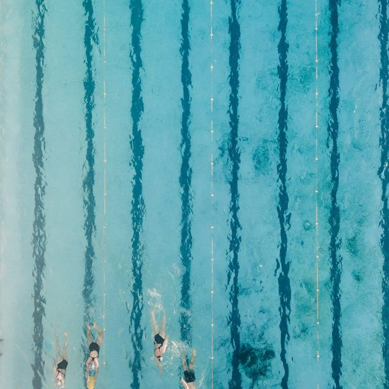 Personen schwimmen im blauen Wasser eines Schwimmbeckens mit klaren Linien.